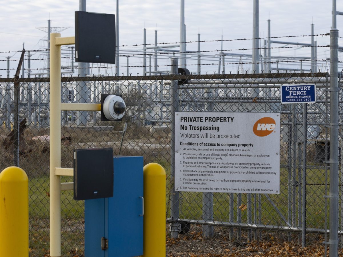 A chain-link fence topped with barbed wire surrounds electrical equipment, with security cameras and a sign reading “PRIVATE PROPERTY No Trespassing Violators will be prosecuted”