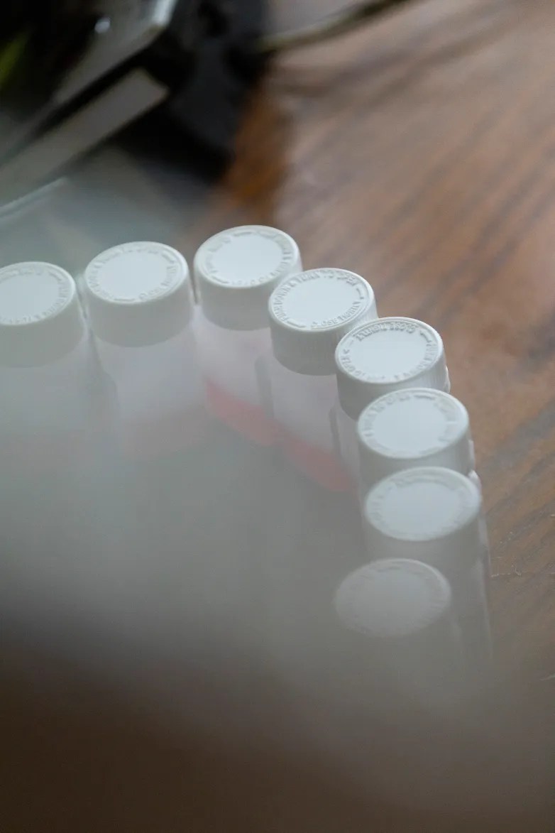 Small bottles with white caps are arranged in a semicircle on a wooden surface, with red liquid visible inside some of the bottles.
