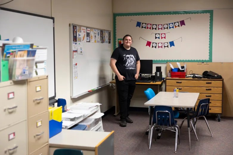 A person wearing a T-shirt with an astronaut graphic stands in a classroom with desks, a whiteboard and a banner reading "WELCOME TO WIN"