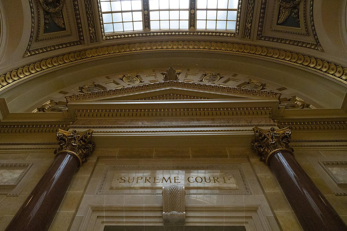 Ornate columns and carved stone surround an entrance marked "SUPREME COURT" beneath a decorative ceiling and skylight.