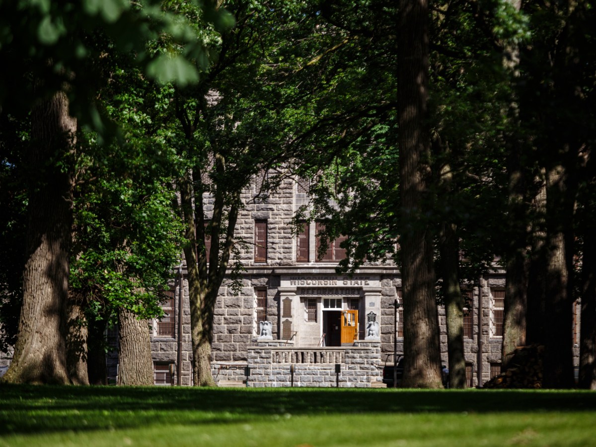 A stone building with “Wisconsin State Reformatory” above the entrance stands behind tall trees and a grassy lawn.